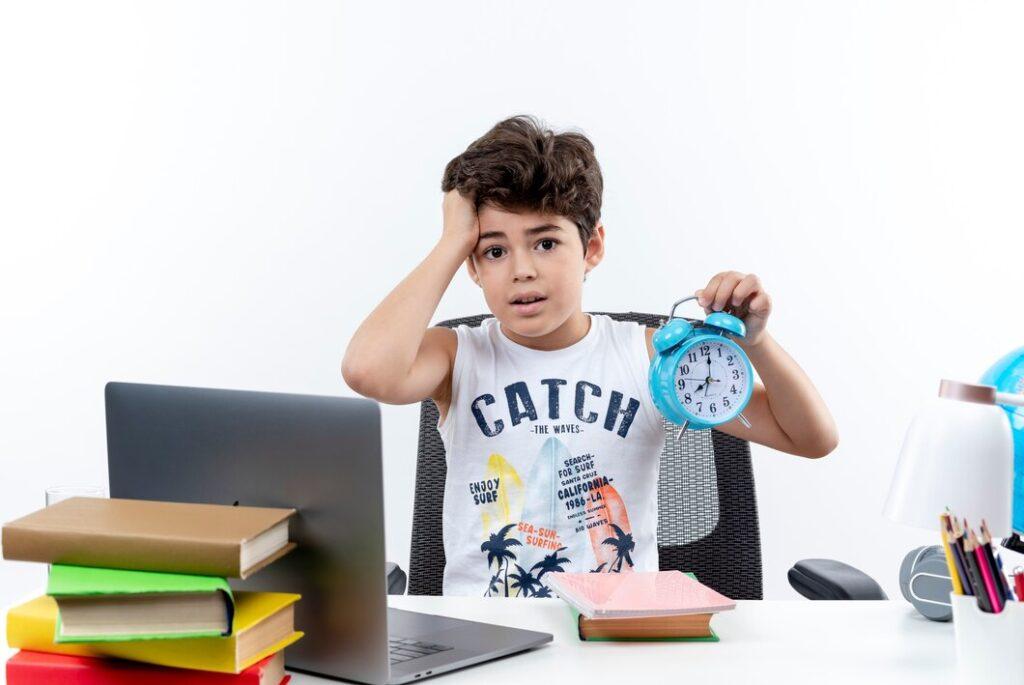 concerned little schoolboy sitting desk with school tools holding alarm clock grabbed head isolated white background 141793 63618