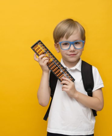 Cute little child kid standing with abacus scores mental arithmetic on yellow background